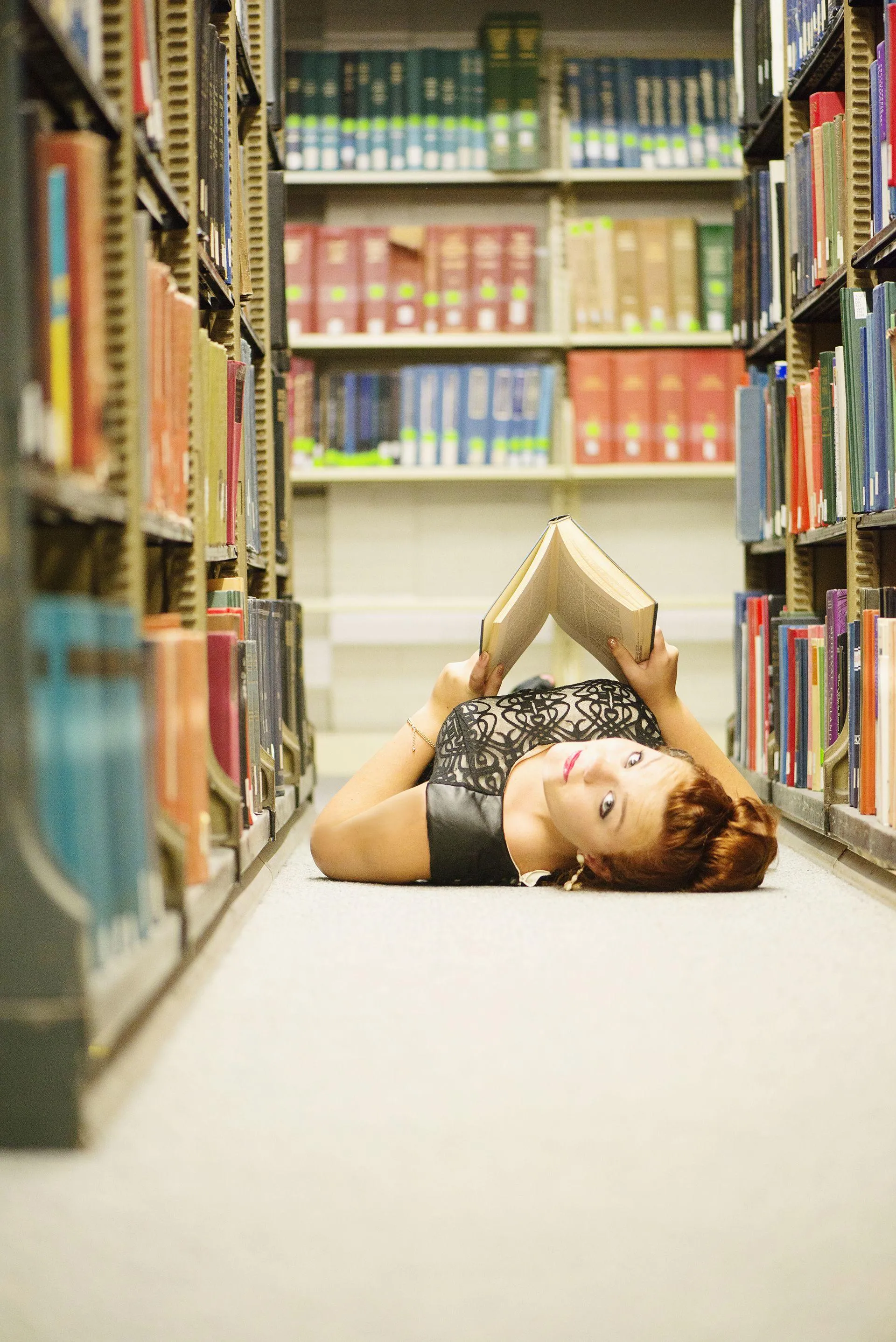 Young Woman Lying on Floor Between Bookshelves in Library