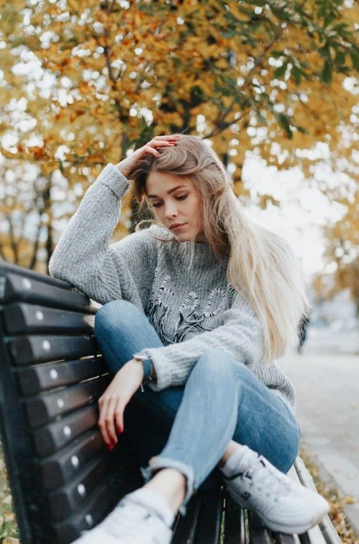 Young Woman Sitting on Bench Surrounded by Autumn Trees