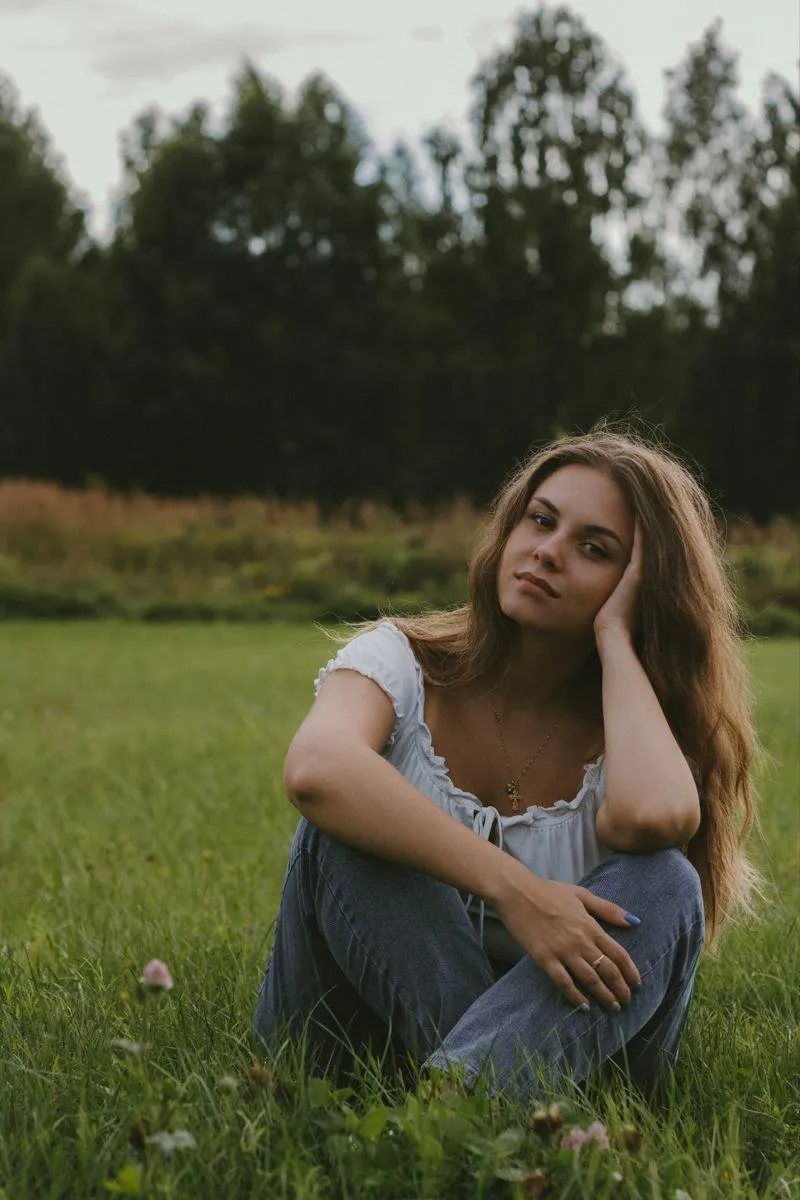 Young Woman Sitting on Grass Lost in a Deep Thoughtful Mood