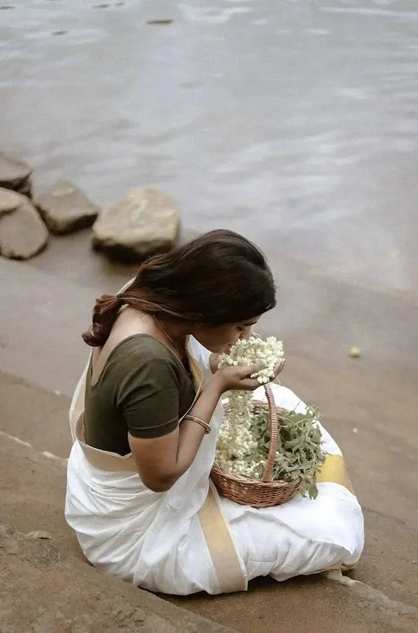 Young woman sitting near the water smelling a jasmine flower