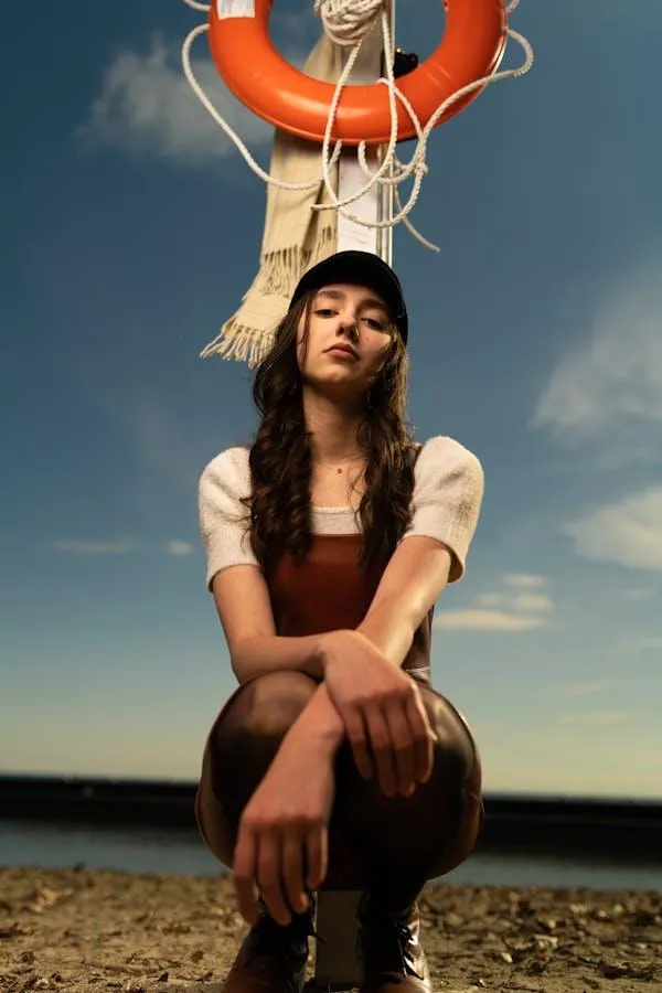 Young Woman Sitting Under Lifebuoy by the Beach on Sunny Day
