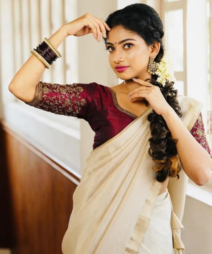 Young woman standing near a window wearing a white saree