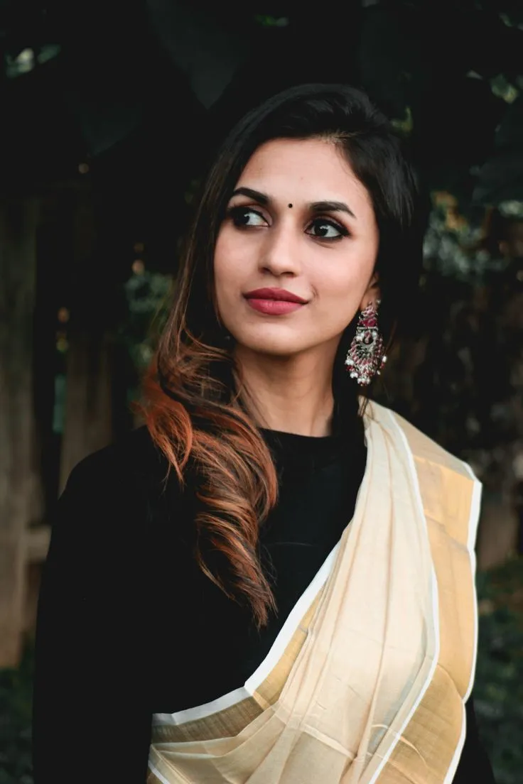 Young woman standing near green leaves wearing a white saree