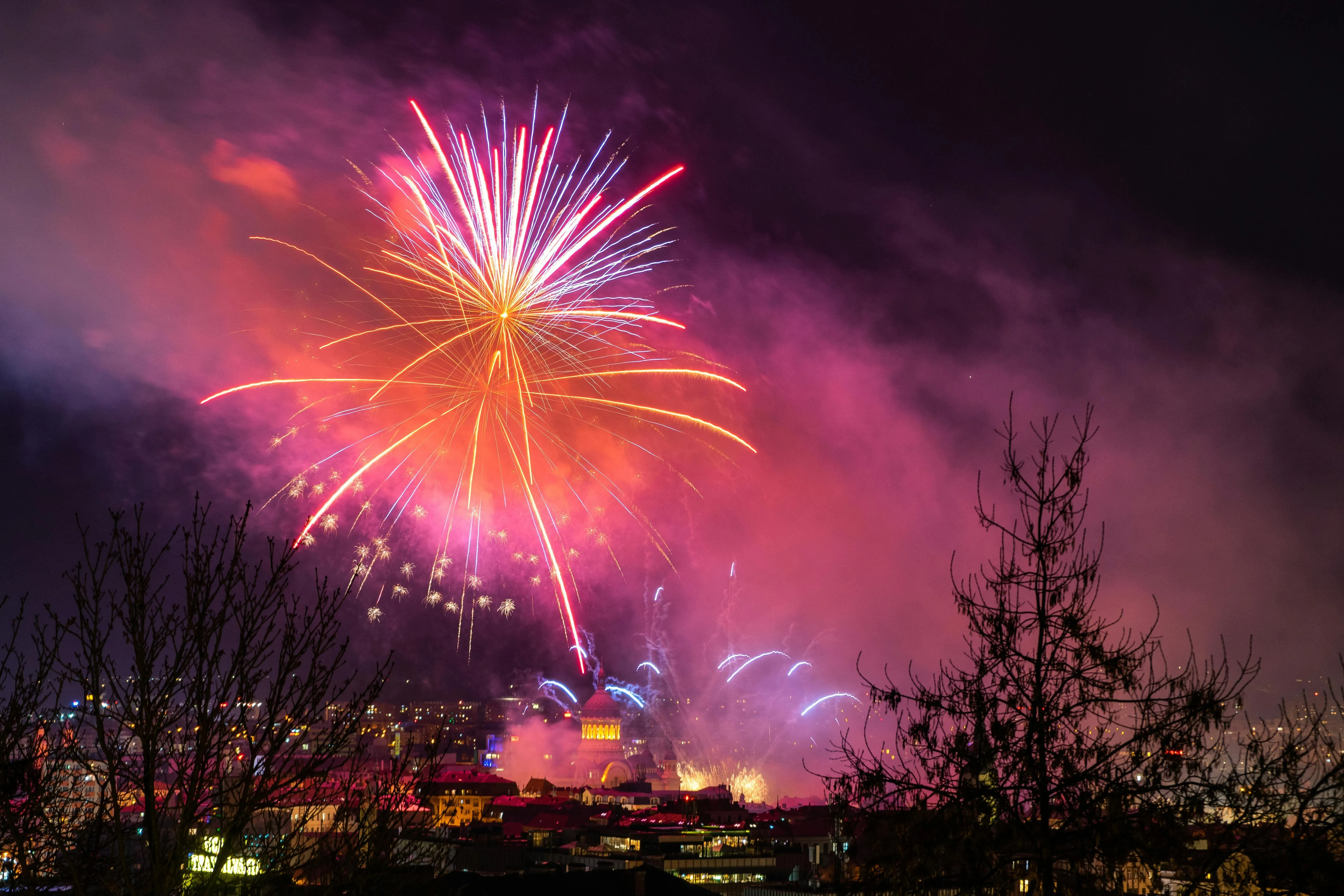 Bright fireworks over a city with a purple glow in the sky