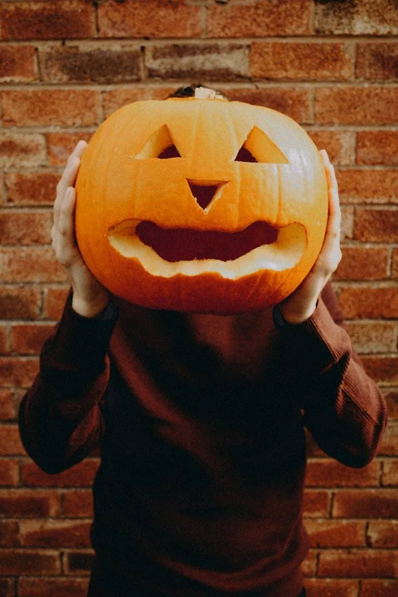 Child Wearing Pumpkin Head Mask Against Brick Wall HD image
