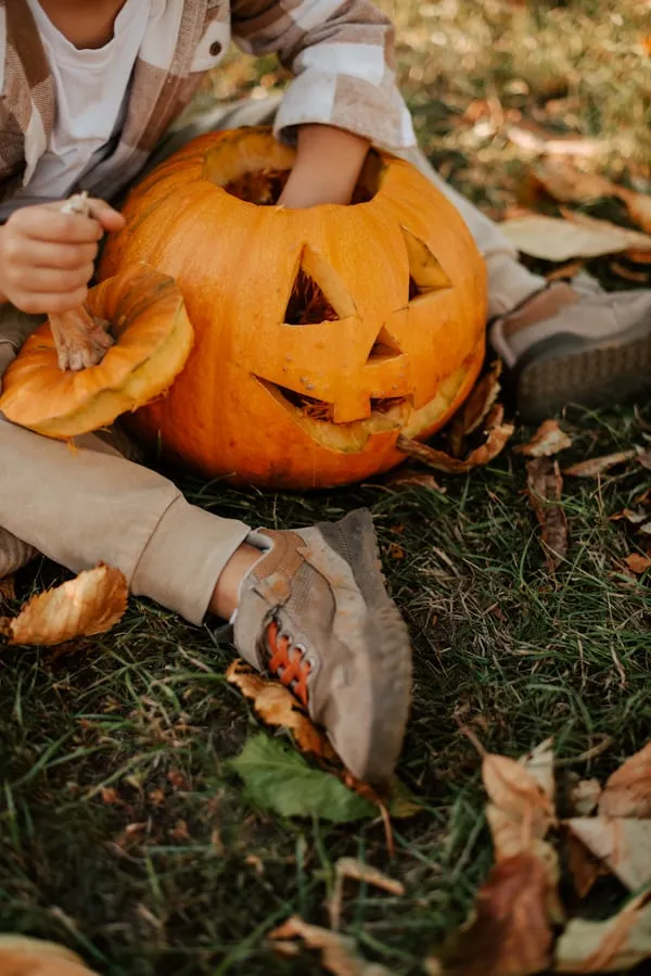 Close Up Of Hand Holding Carved Pumpkin on Autumn Leaves
