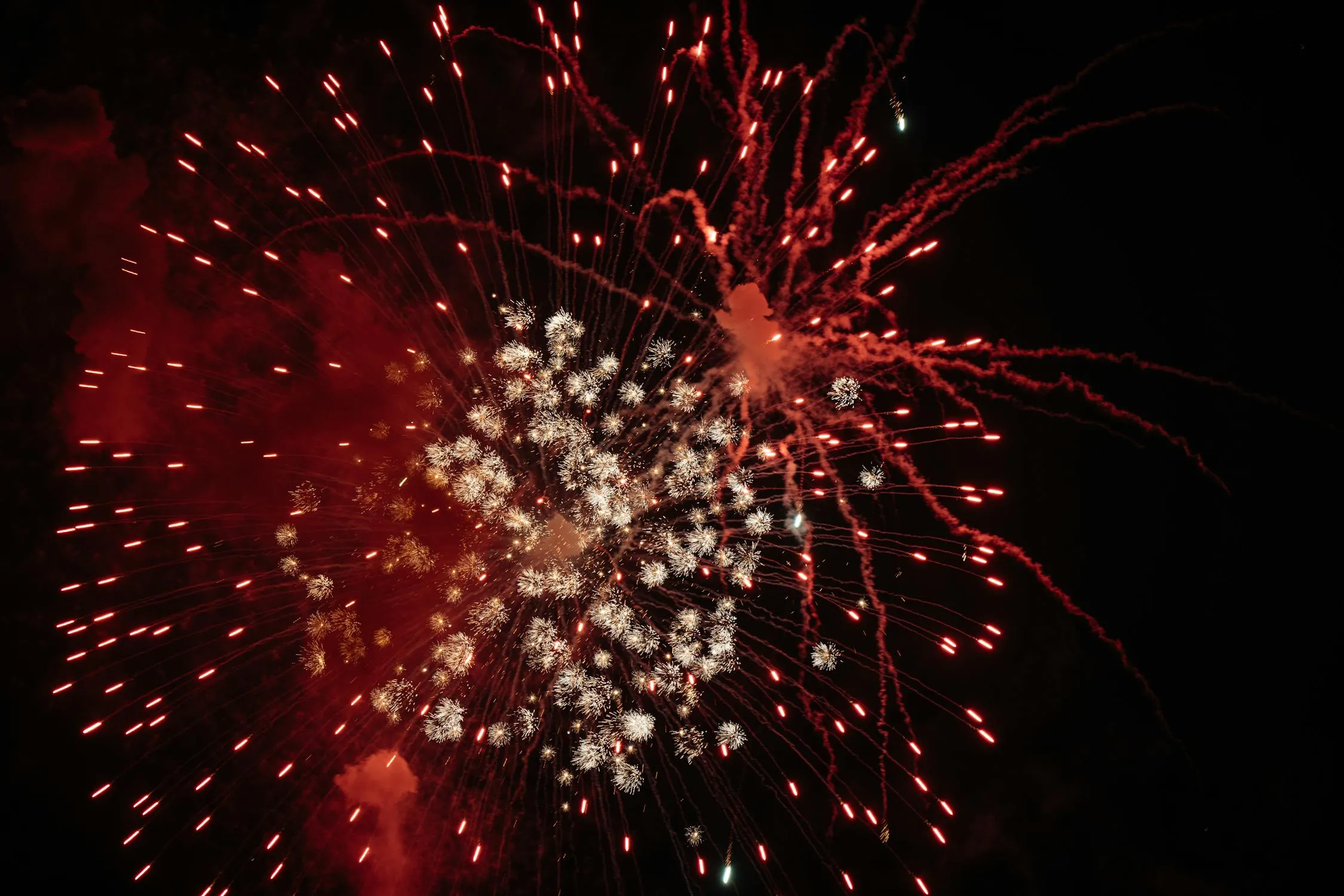 Close up red and white fireworks exploding in dark sky