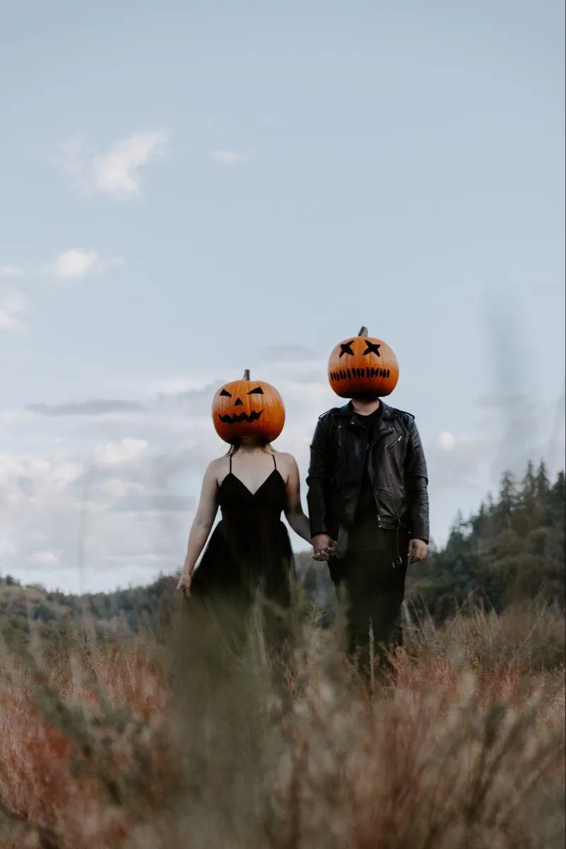 Couple in field with pumpkin heads holding hands gently