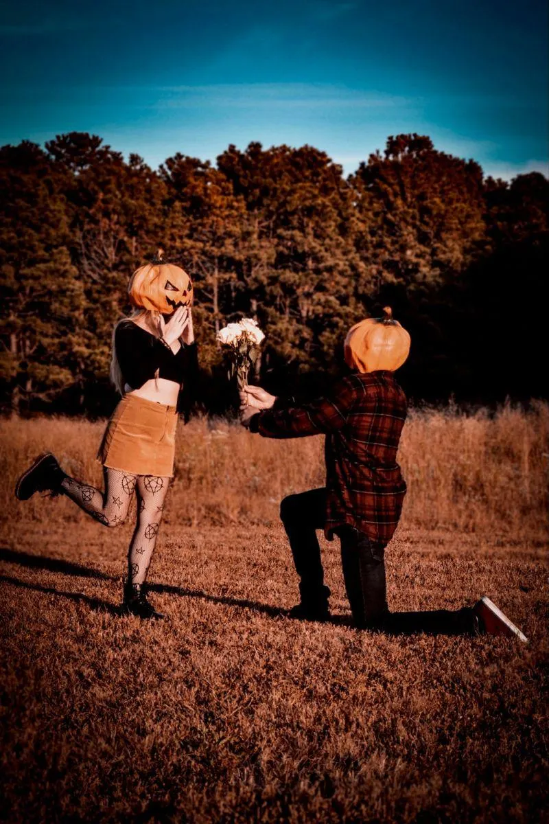 Couple proposing with Pumpkin Heads in Fall Field image