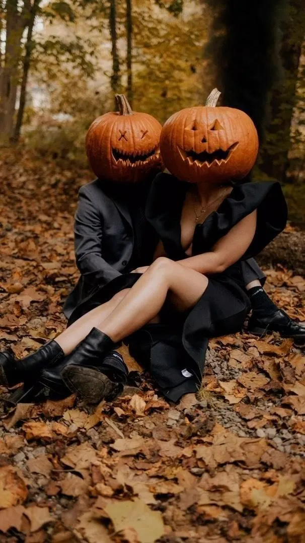 Couple Wearing Pumpkin Heads Sitting on Fall Leaves image