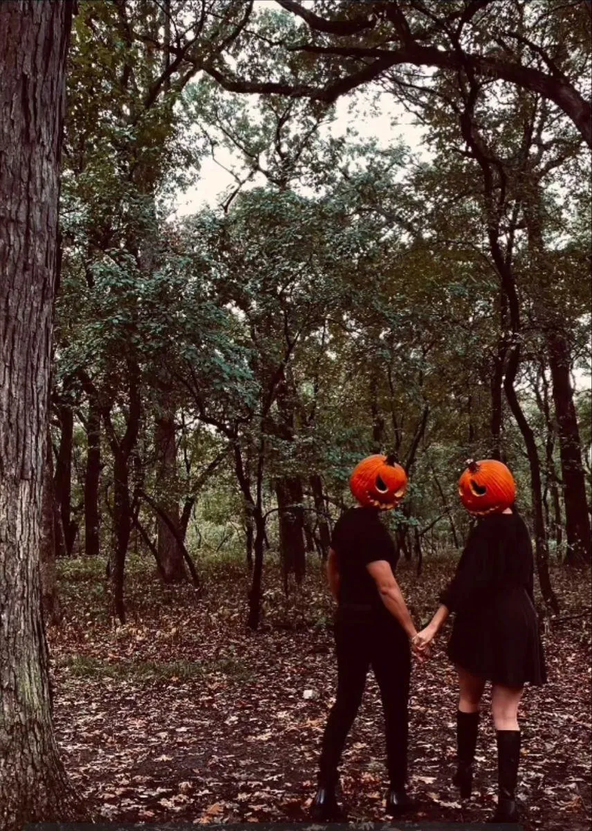 Couple Wearing Pumpkin Masks Holding Hands in Autumn Forest