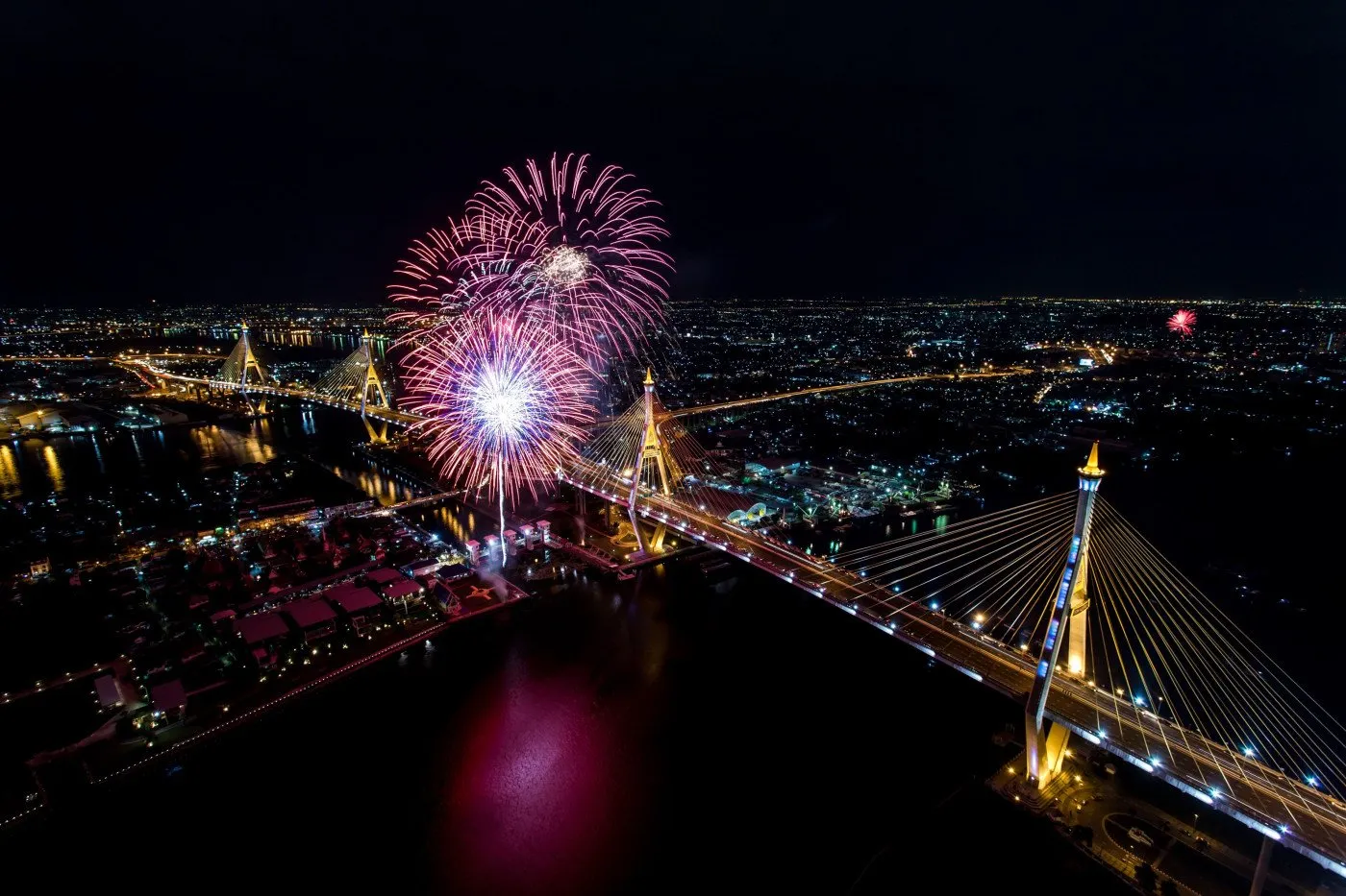 Fireworks over illuminated bridge and glowing urban night