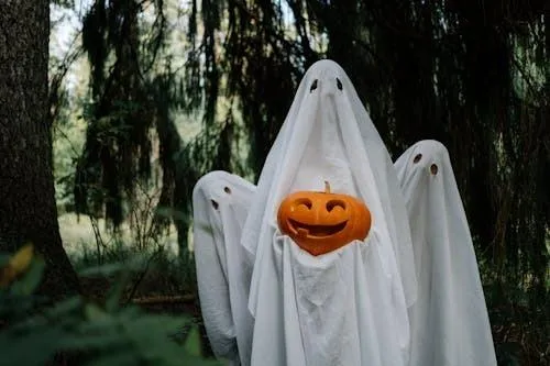 Ghost Costume Holding Pumpkin Outdoors in Autumn Forest