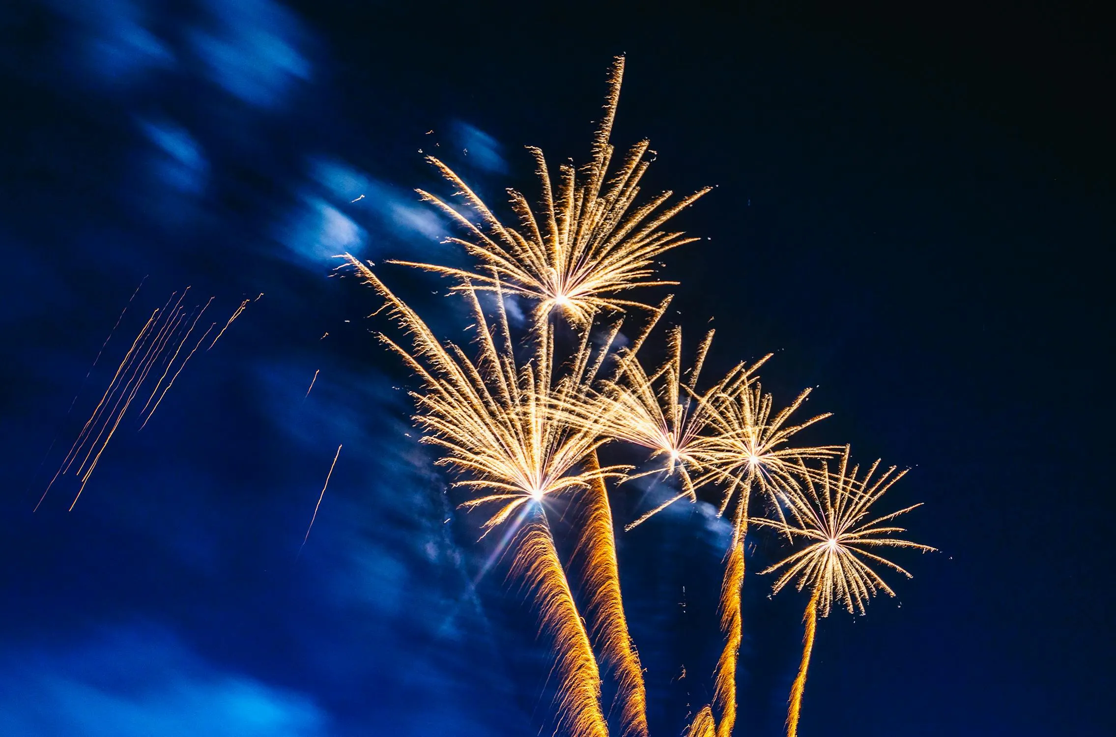Golden fireworks burst across deep blue night background