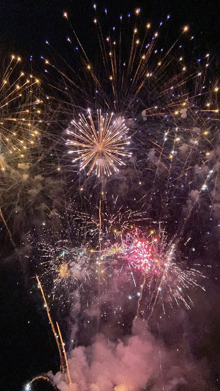 Golden fireworks explode in the sky above smoky clouds