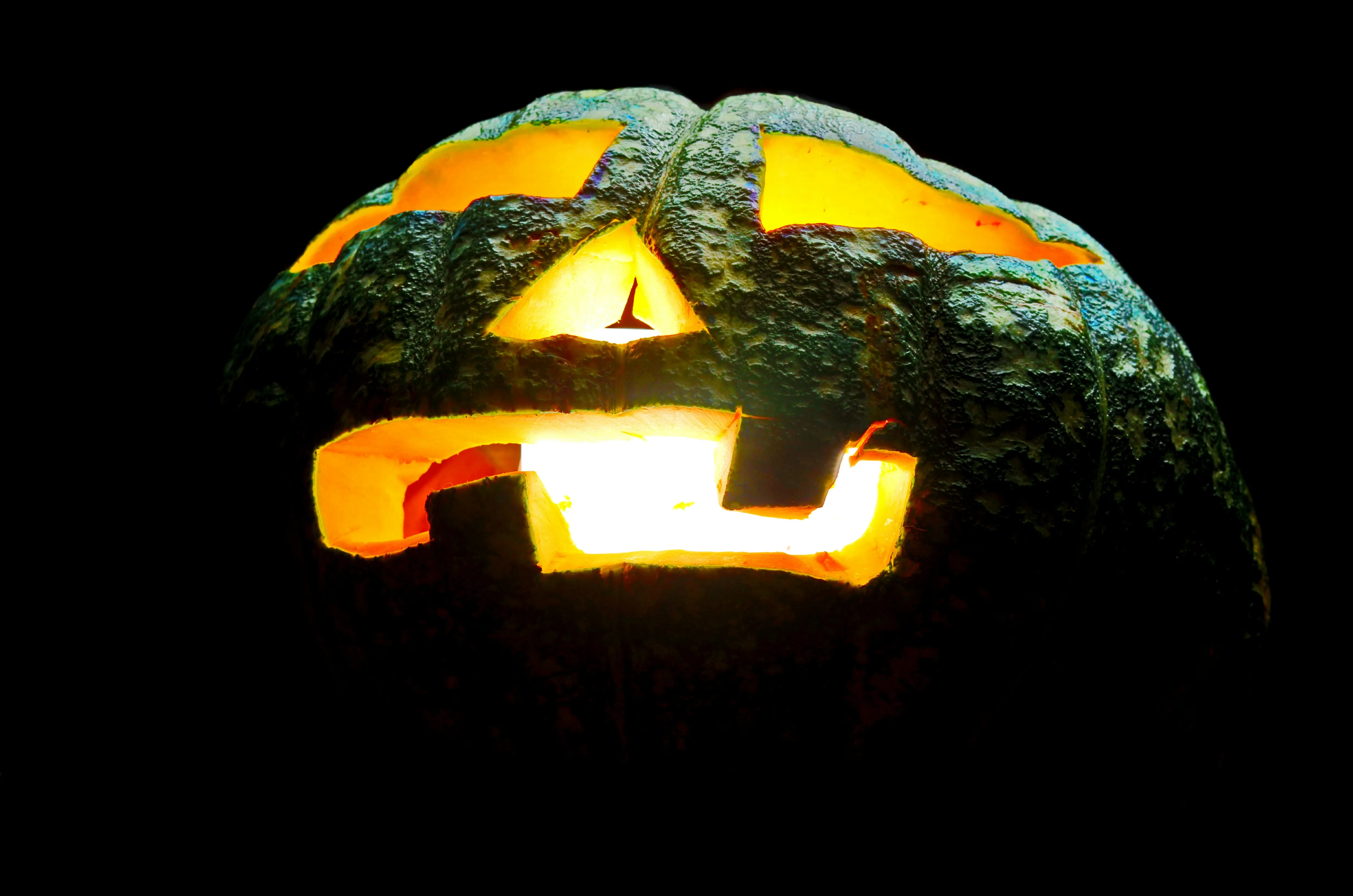 Green Pumpkin with Creepy Face Carving Glowing at Night