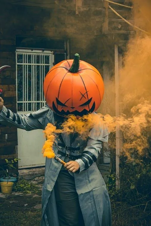 Halloween person with pumpkin mask holding Orange smoke