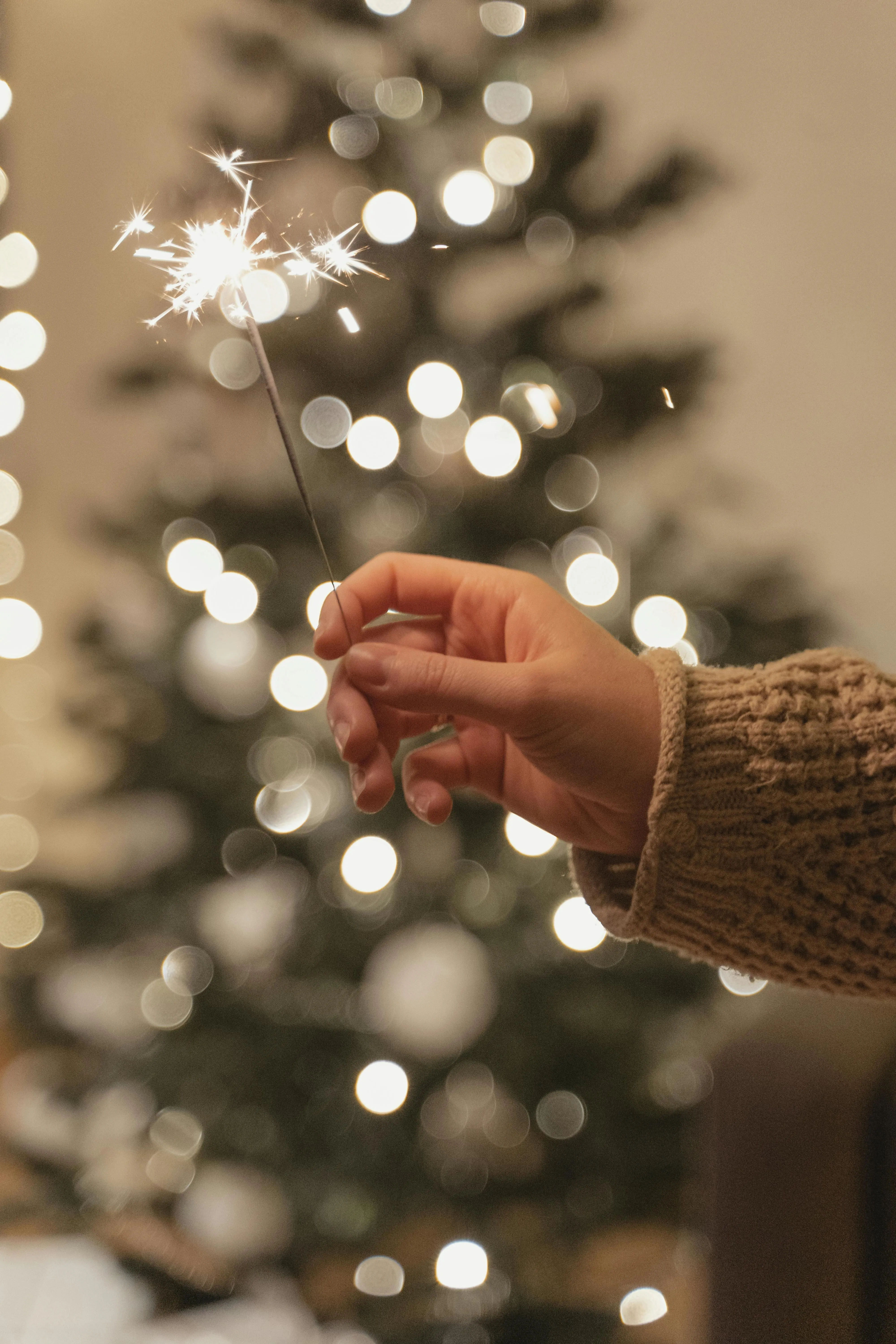 Hand Holding a Sparkler in Front of a Lit Christmas Tree