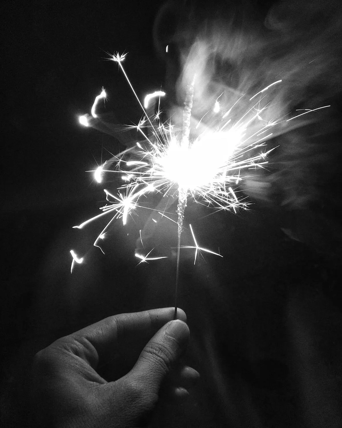 Hand holding sparkler with blurry fireworks in the back