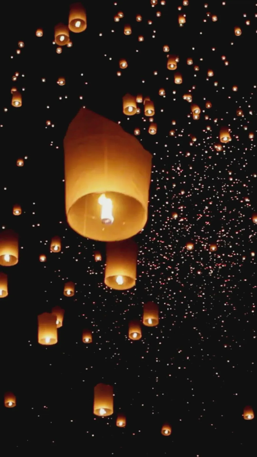 Lanterns floating up into the dark sky with sparkling lights