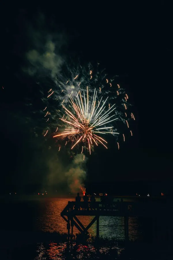 Large Firework Bursts Near Pier with Reflections on the Water