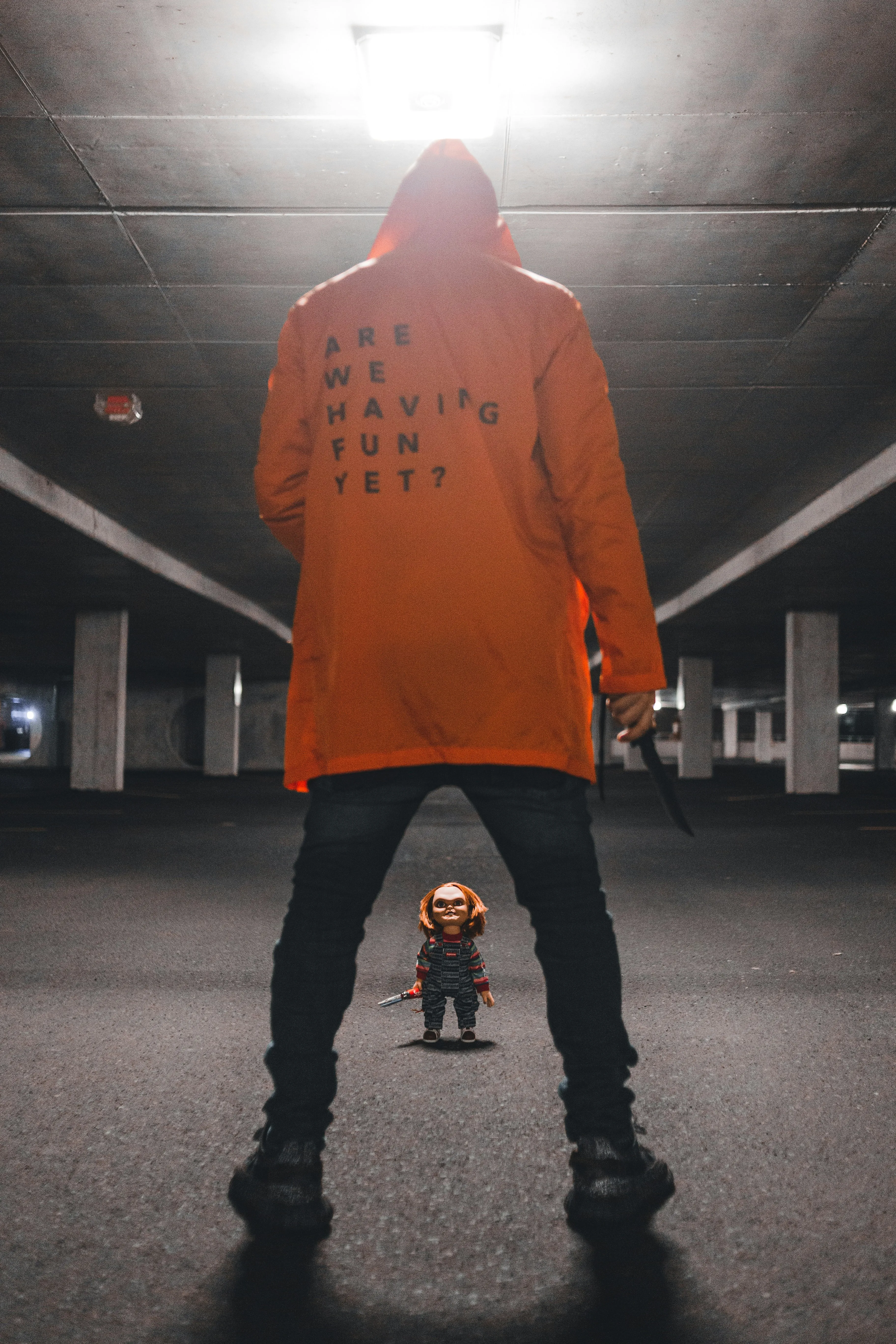Man in Hoodie Faces Chucky Doll in Dark Parking Garage
