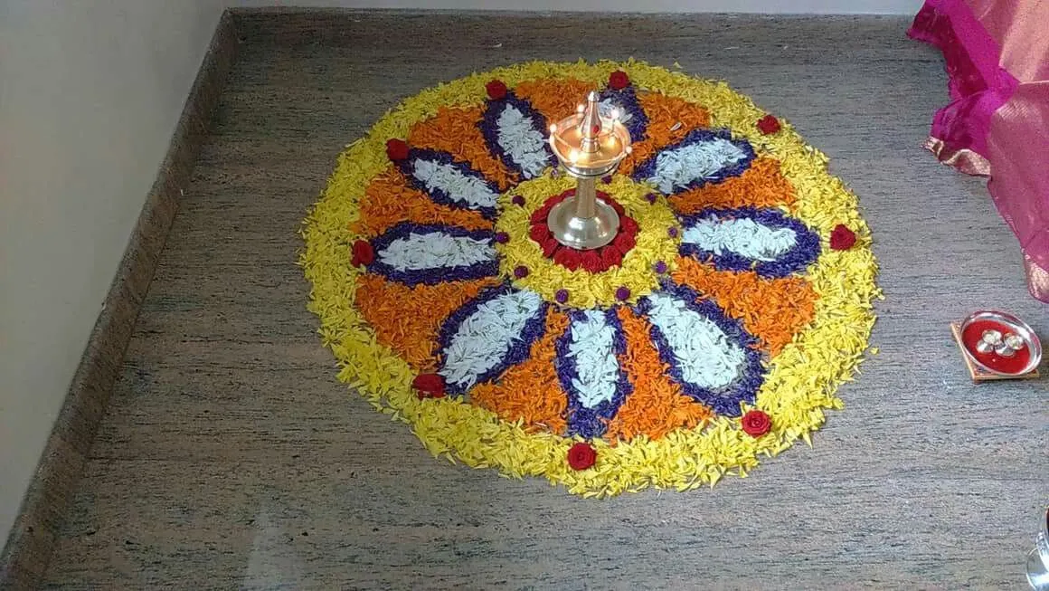 Onam floral rangoli art with a yellow circular base and lamp
