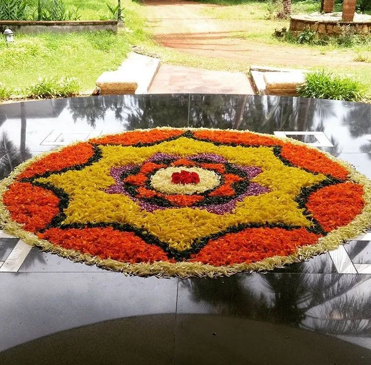 Orange circular pookolam with a yellow star on a black floor