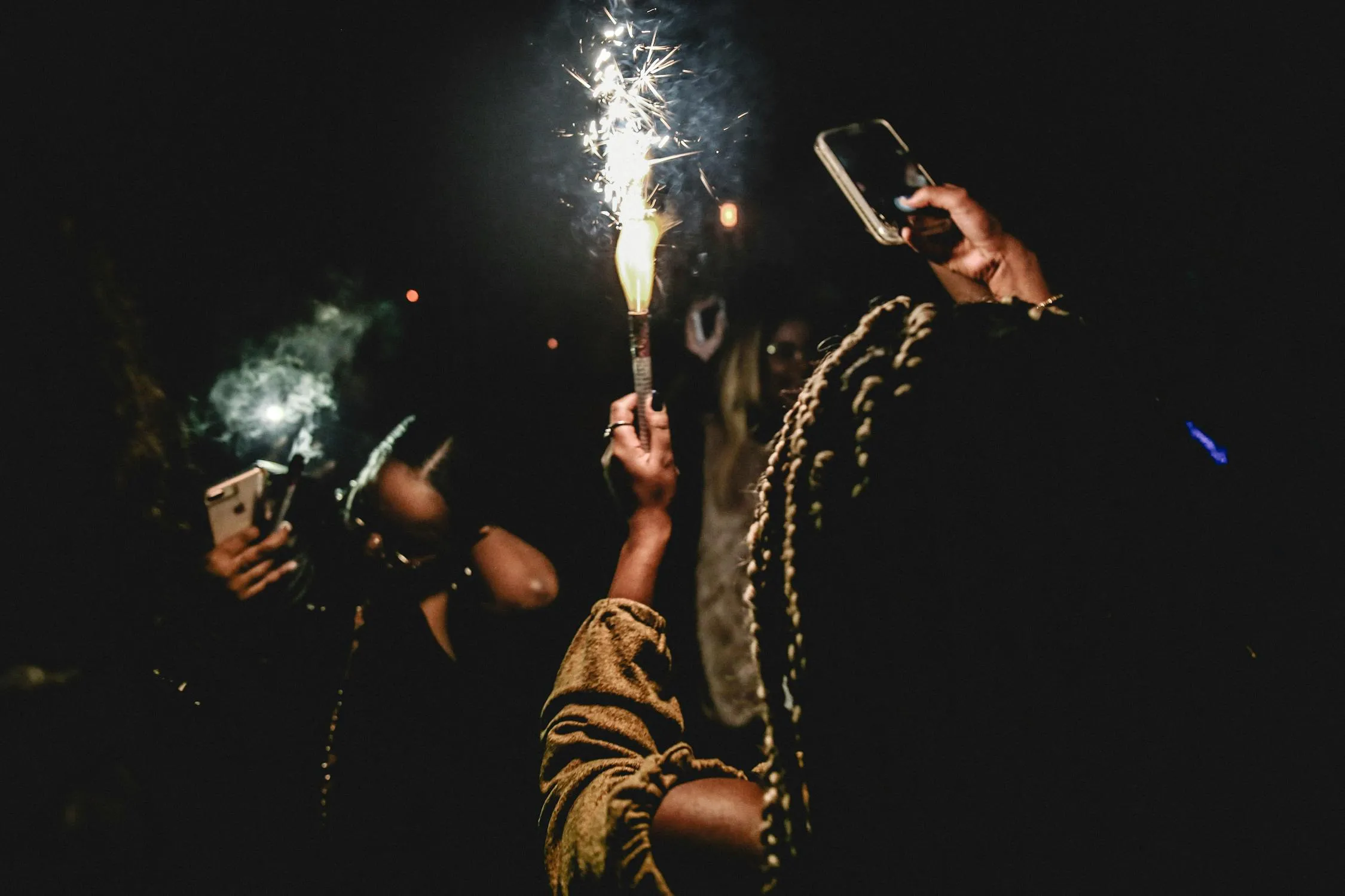People holding sparklers with fireworks in the background