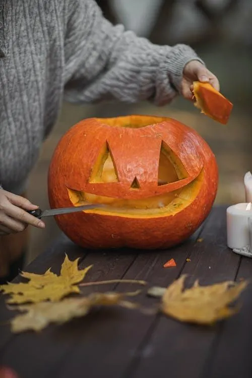 Person Carving Pumpkin with Autumn Leaves on Table