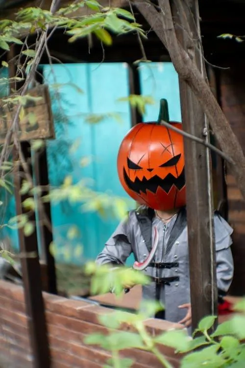 Person in Halloween costume with a pumpkin head near plants