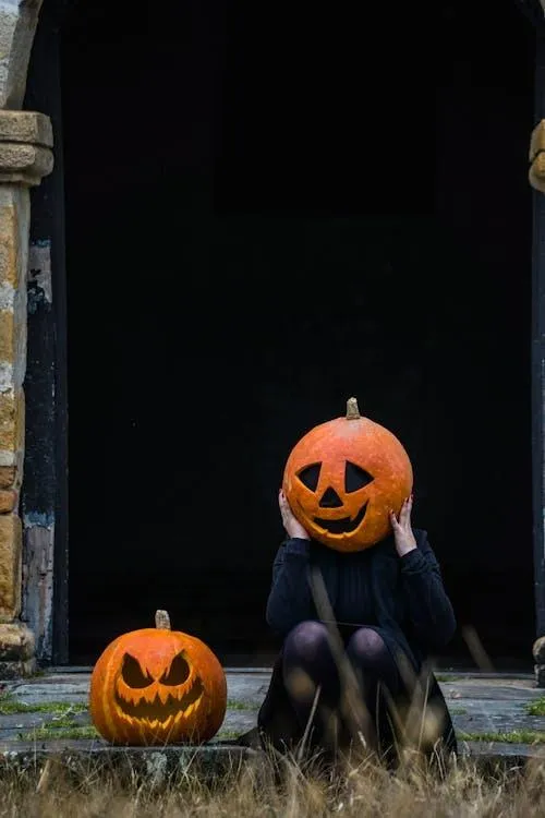 Person in Pumpkin Head Costume Posing near Haunted House