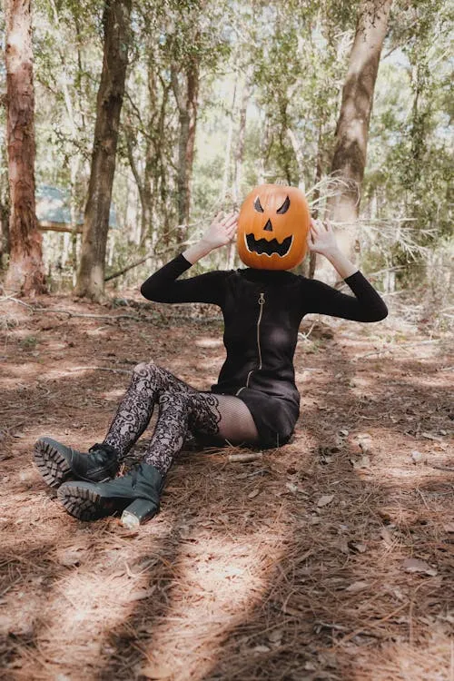 Person Sitting on Ground Wearing Black Outfit and Pumpkin Head