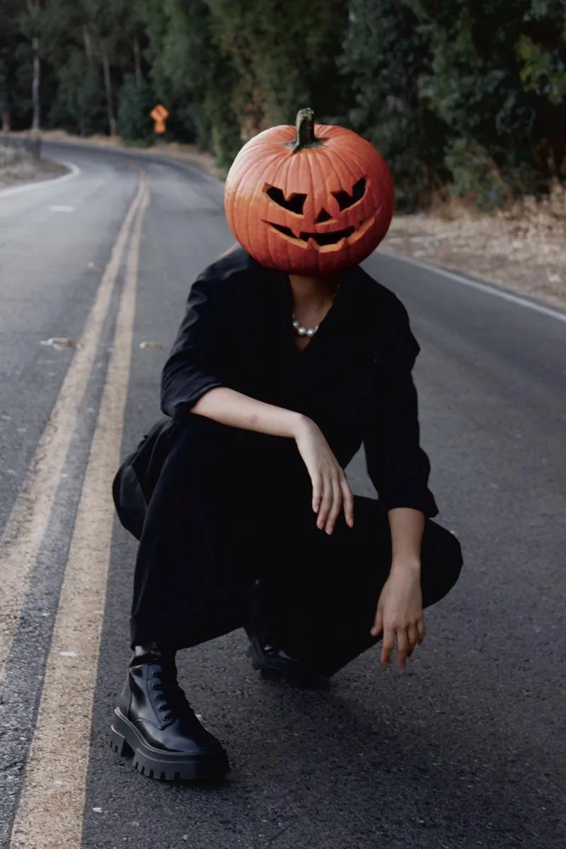 Person Squatting on Road Wearing Pumpkin Head Mask image