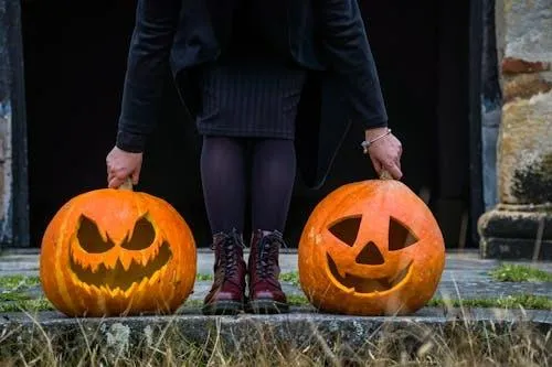 Person Standing with Two Carved Pumpkins on Autumn Pathway
