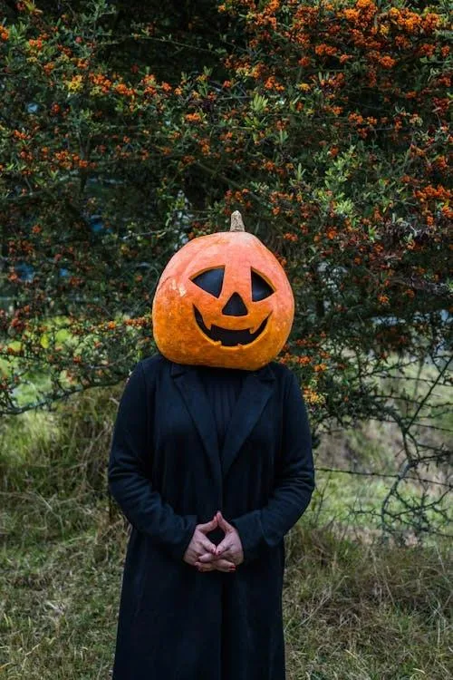 Person Wearing Pumpkin Head in Quiet Outdoor Setting
