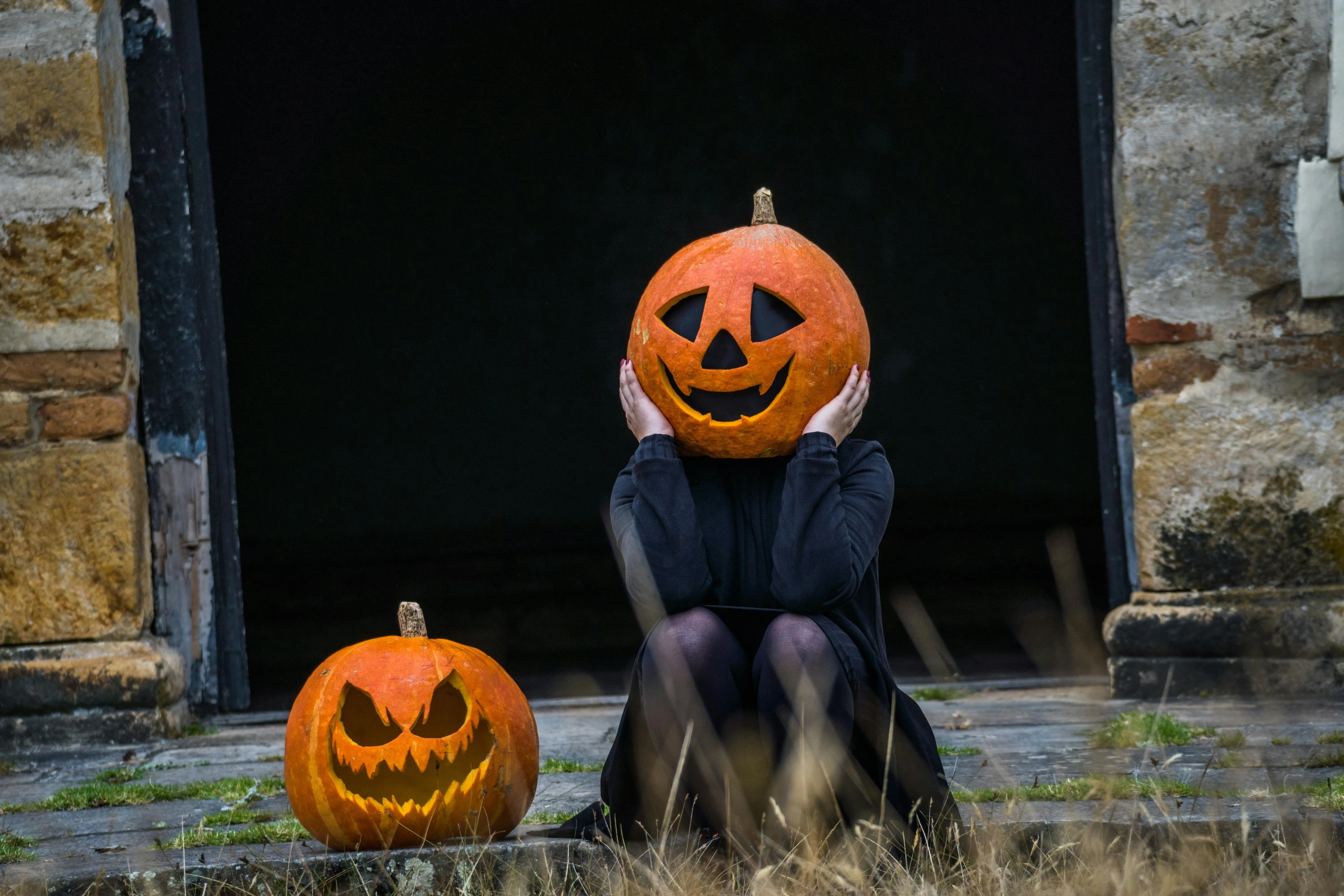 Person Wearing Pumpkin Head Sitting on Stone Steps