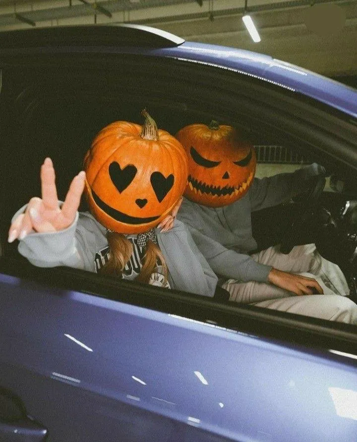 Person Wearing Pumpkin Mask Making Peace Sign From Car Window