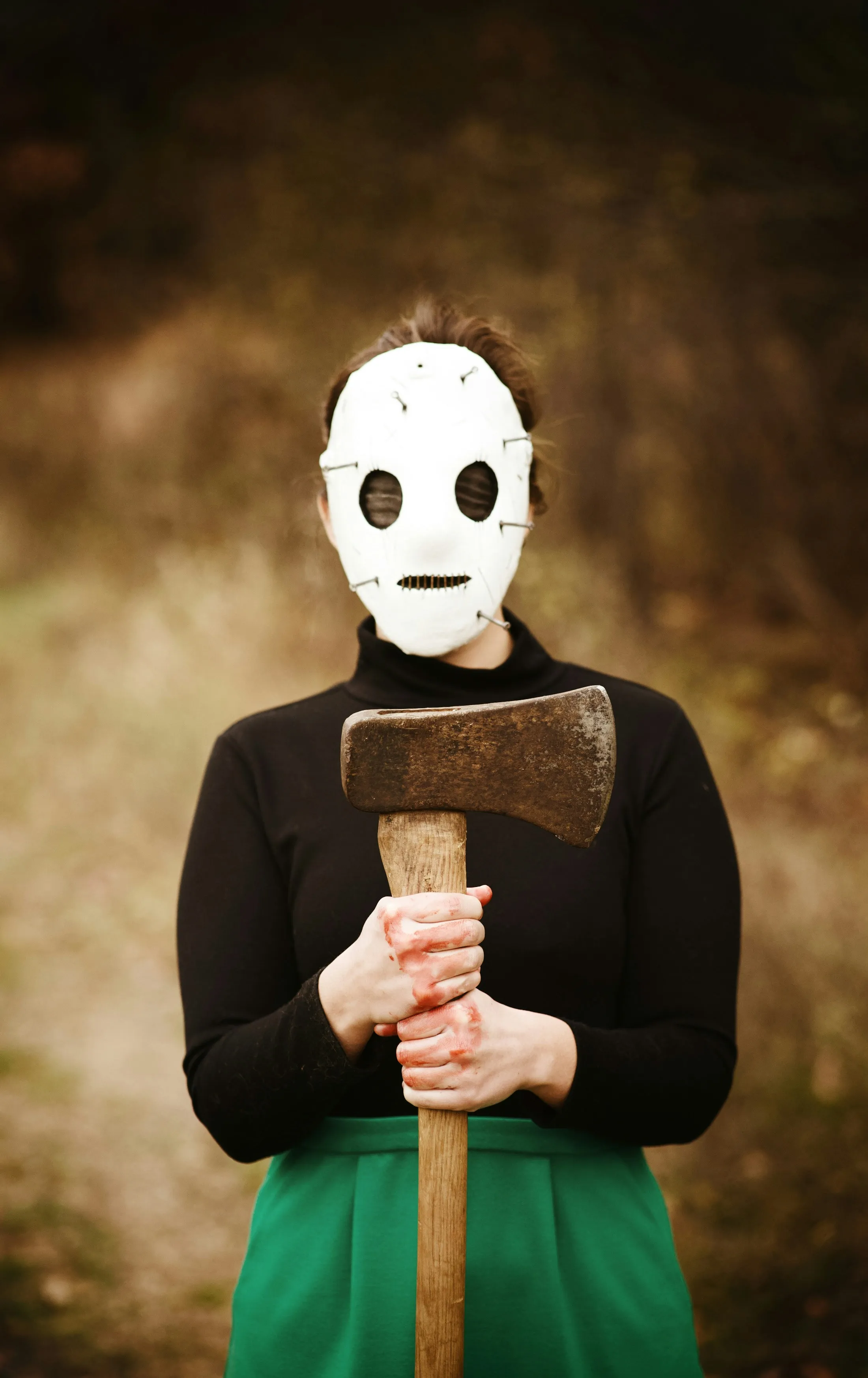 Person Wearing White Mask Holding Axe in Dark Setting