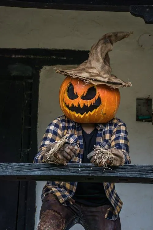 Person with pumpkin head wearing a scarecrow hat near balcony