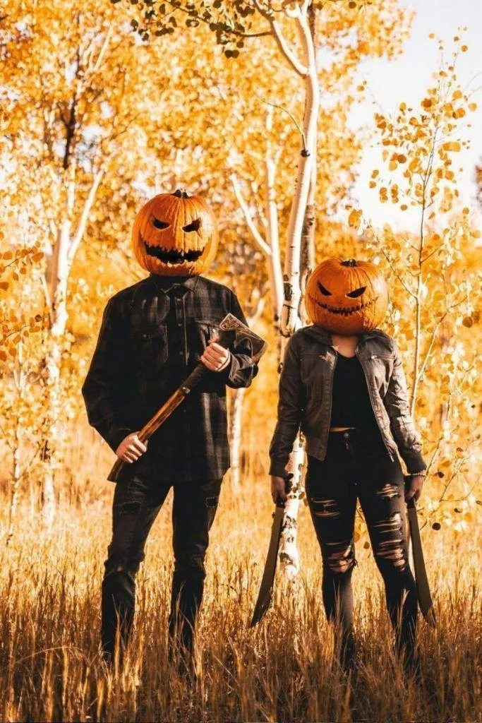 Pumpkin Head Couple Standing in Fall Leaves with Axe