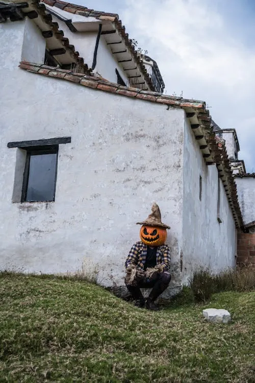 Pumpkin head person sitting near white building outdoors