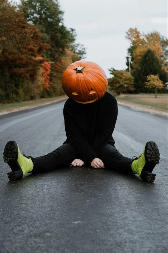 Pumpkin head person sitting on a road with legs spread