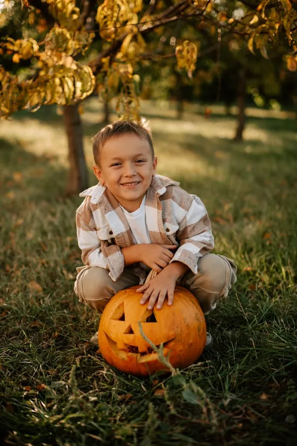 Smiling Child Holding Pumpkin in Sunny Autumn Park Wallpaper