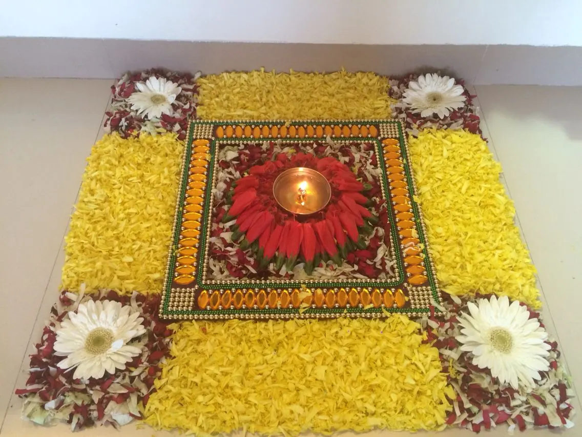 Square Onam Athapookolam with a glowing oil lamp at center