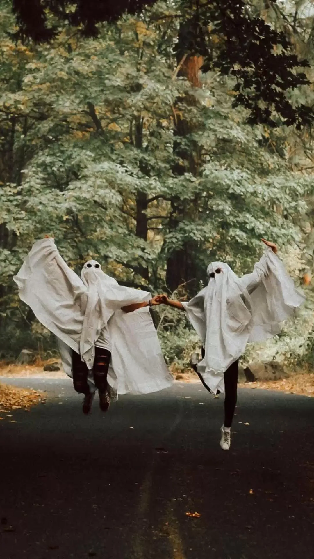 Two Friends Jumping in Ghost Costumes on Forest Road