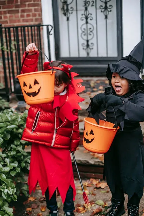 Two kids dressed in Halloween costumes holding buckets