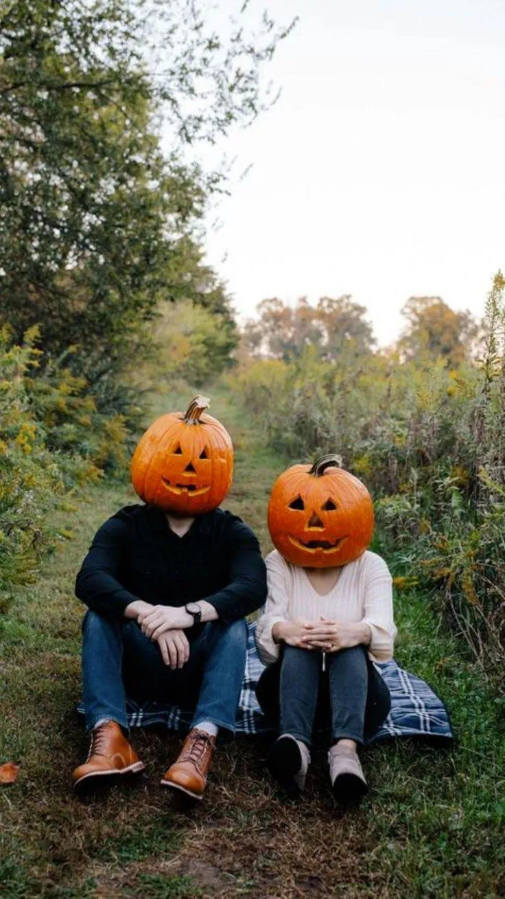 Two Kids Wearing Pumpkin Heads Sitting Outdoors 4K image