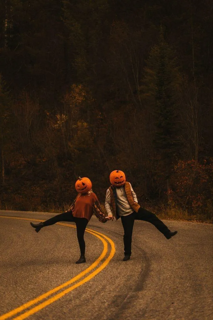 Two People Dancing on Road with Pumpkin Head Masks at Sunset