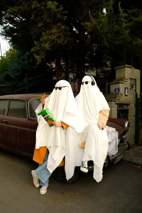 Two People Dressed as Ghosts sitting above car image